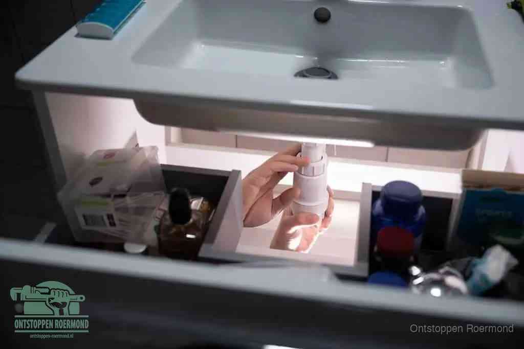 Een pompfles met zeep boven een wastafel, de heet water en afwasmiddel-methode om een vetprop in de afvoer los te maken in Roermond