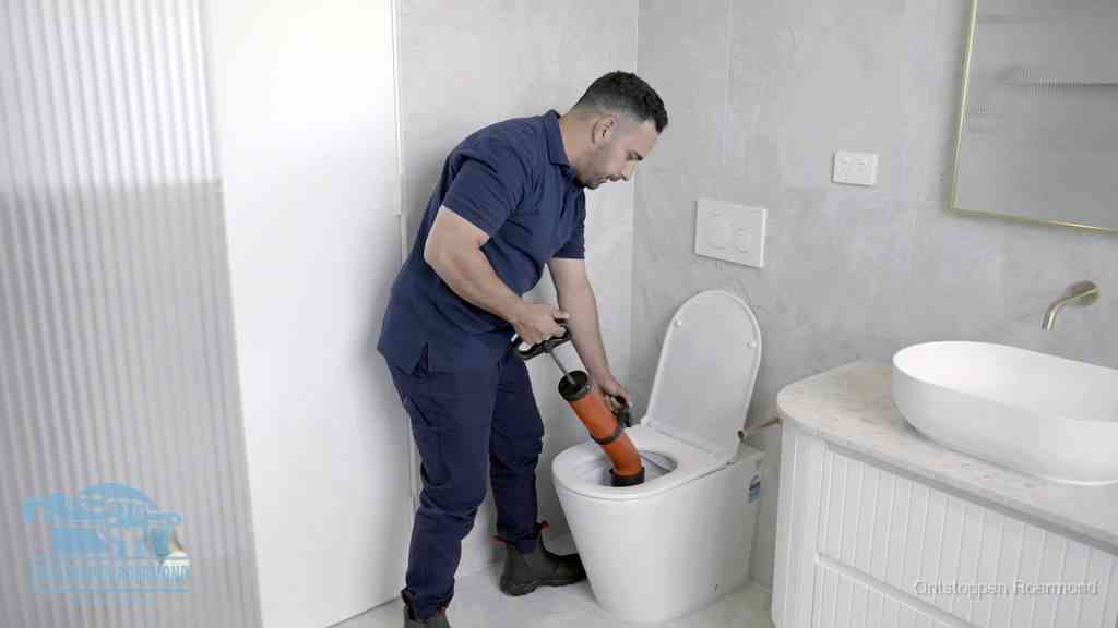 Een monteur buigt over een wandcloset en duwt met de hand een persluchtontstopper in de toiletpot om de verstopping handmatig los te maken in Roermond