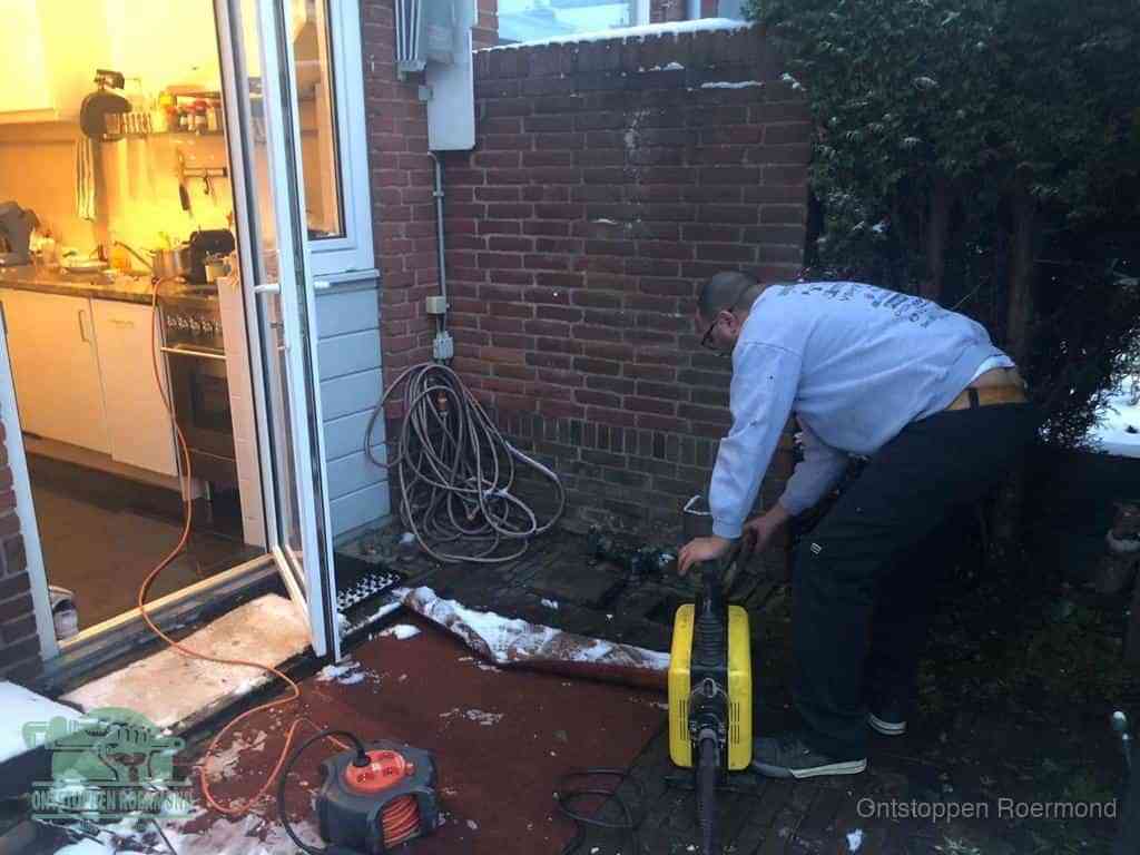 Een monteur werkt buiten bij een open riool-/grondput met een elektrische ontstoppingsmachine om een verborgen afvoerprobleem op te sporen in Roermond