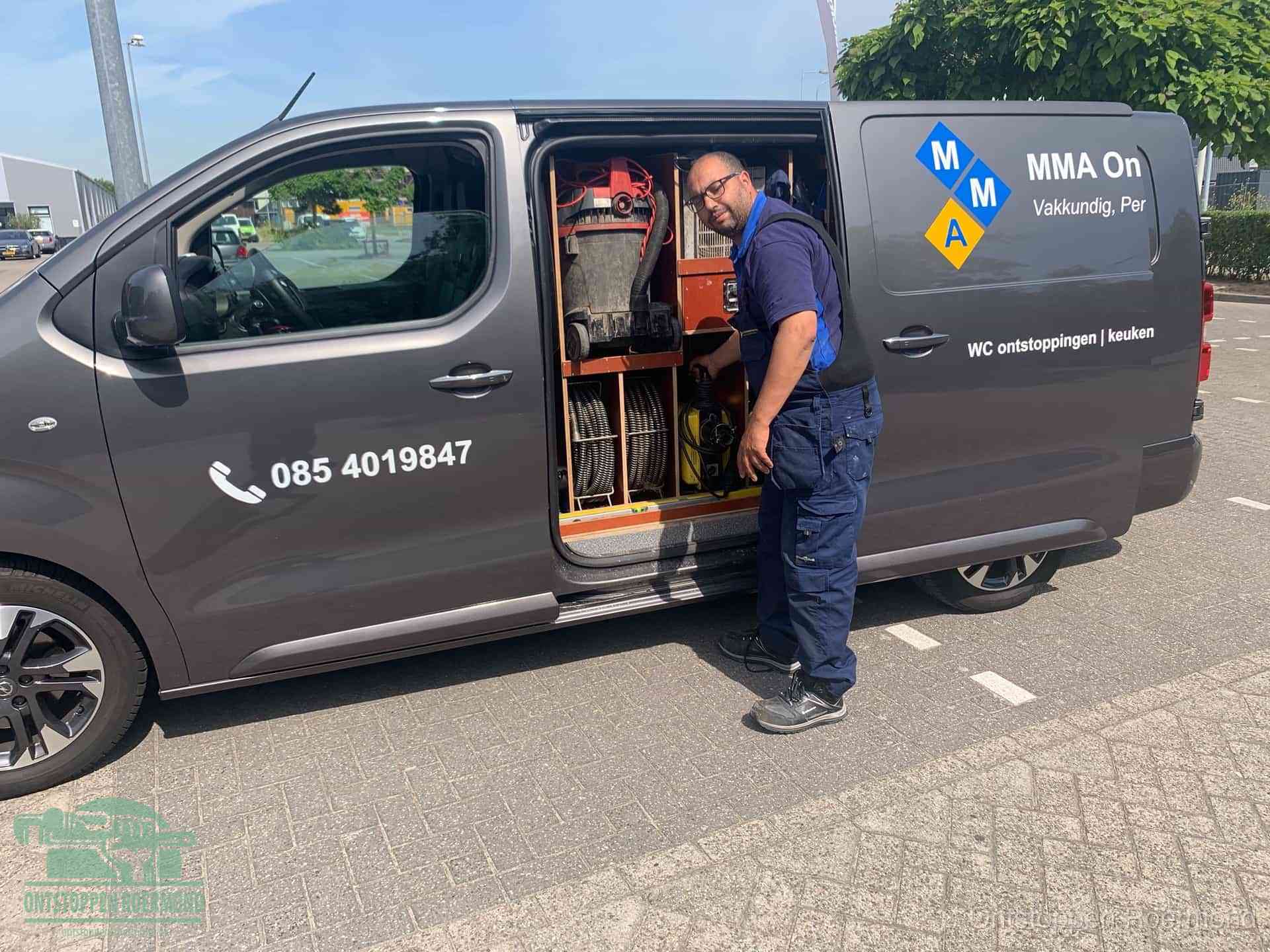 Een monteur bij de open schuifdeur van zijn bedrijfsbus op een parkeerplaats, klaar om de oorzaak van terugkerende afvoerverstoppingen aan te pakken in Roermond