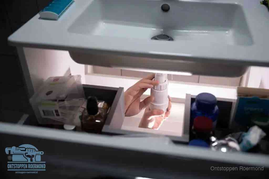 Een pompfles met zeep boven een wastafel in de toiletruimte, de warm water en afwasmiddel-methode om de wc te ontstoppen in Roermond