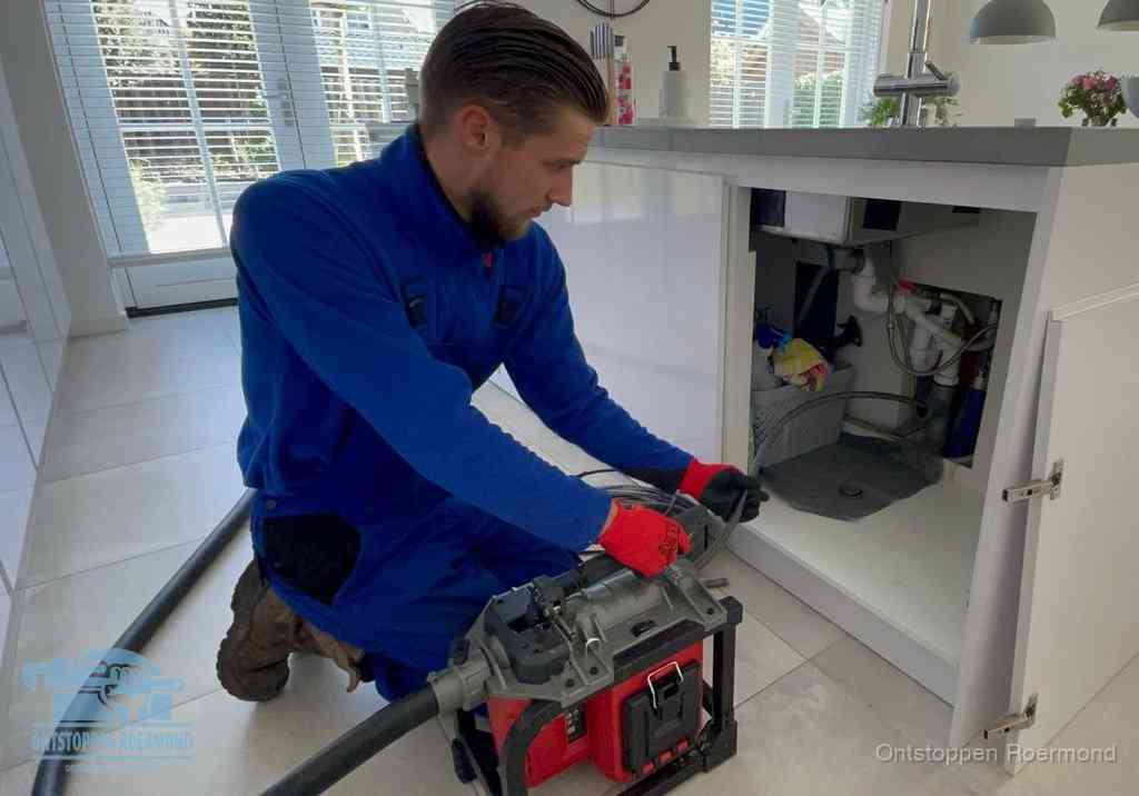Een monteur voert een professionele elektrische ontstoppingsmachine in de afvoer onder de spoelbak tijdens het gootsteen ontstoppen in Roermond