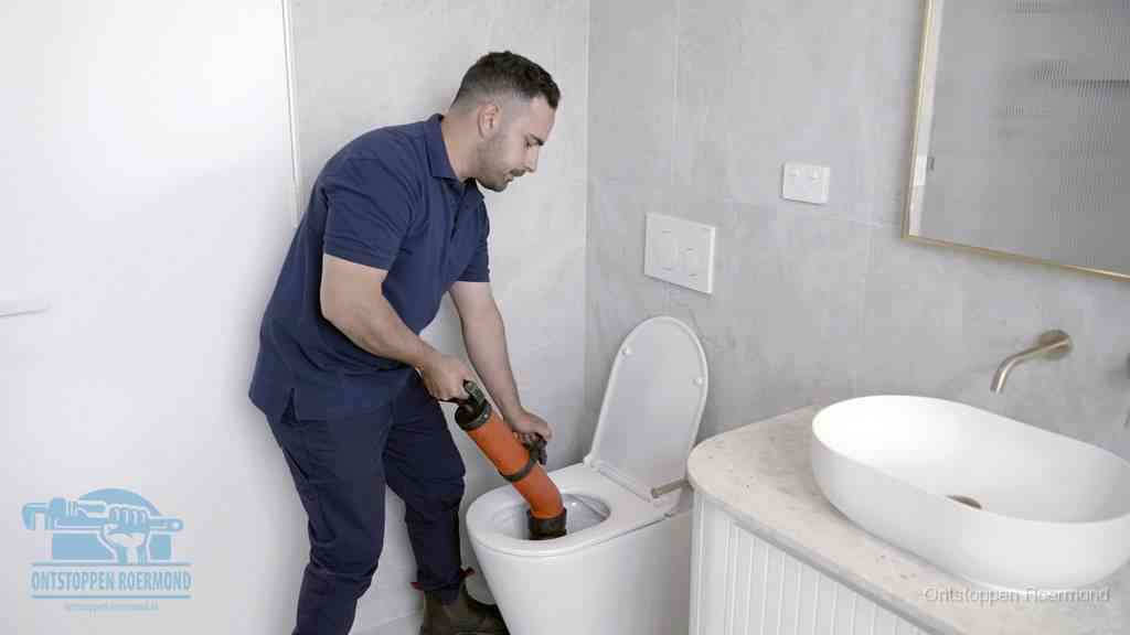 Een man gebruikt een handmatige luchtdruk-ontstopper in een modern betegeld toilet om zelf de wc te ontstoppen in Roermond